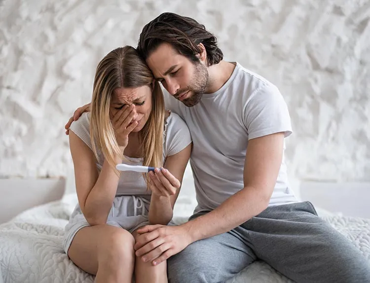 An upset woman holding negative pregnancy test with husband supporting her.